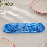 Blue marbled ceramic dish on a light surface with other ceramic items and a plant.