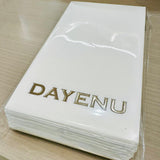 Stack of white napkins with 'DAYENU' embroidered on them, placed on a wooden surface.