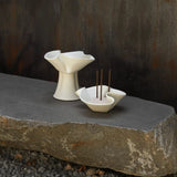 Two white ceramic bowls with incense sticks on a stone slab against a dark background