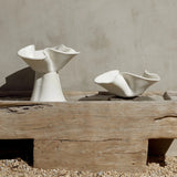 Two white ceramic bowls on a wooden platform against a beige wall.