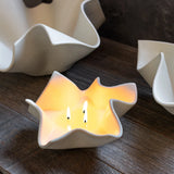 White ceramic candle holders on a wooden surface with one holding a lit candle.