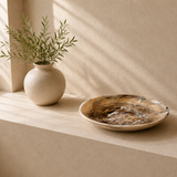 Ceramic items including a vase with plants, a large plate, and a small bowl on a beige surface.