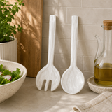 White ceramic salad servers on a kitchen counter with a bowl of salad and oil bottle in the background.