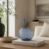 Blue glass vase on a book with a beige bowl and plant in the background