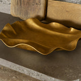 Gold decorative dish on a textured surface with a wooden block in the background