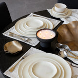 Dining table setting with white ceramic plates, gold cutlery, and a candle.