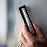 Hand holding a silver pen in a black box against a neutral background