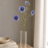 Clear vase with blue flowers on a wooden surface next to books and a bowl.
