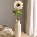 White vase with a single flower on a wooden surface with books and a bowl.