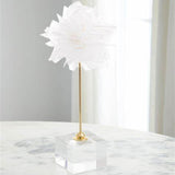 Decorative table lamp with white floral shade and gold base on a clear acrylic block, set against a neutral background.